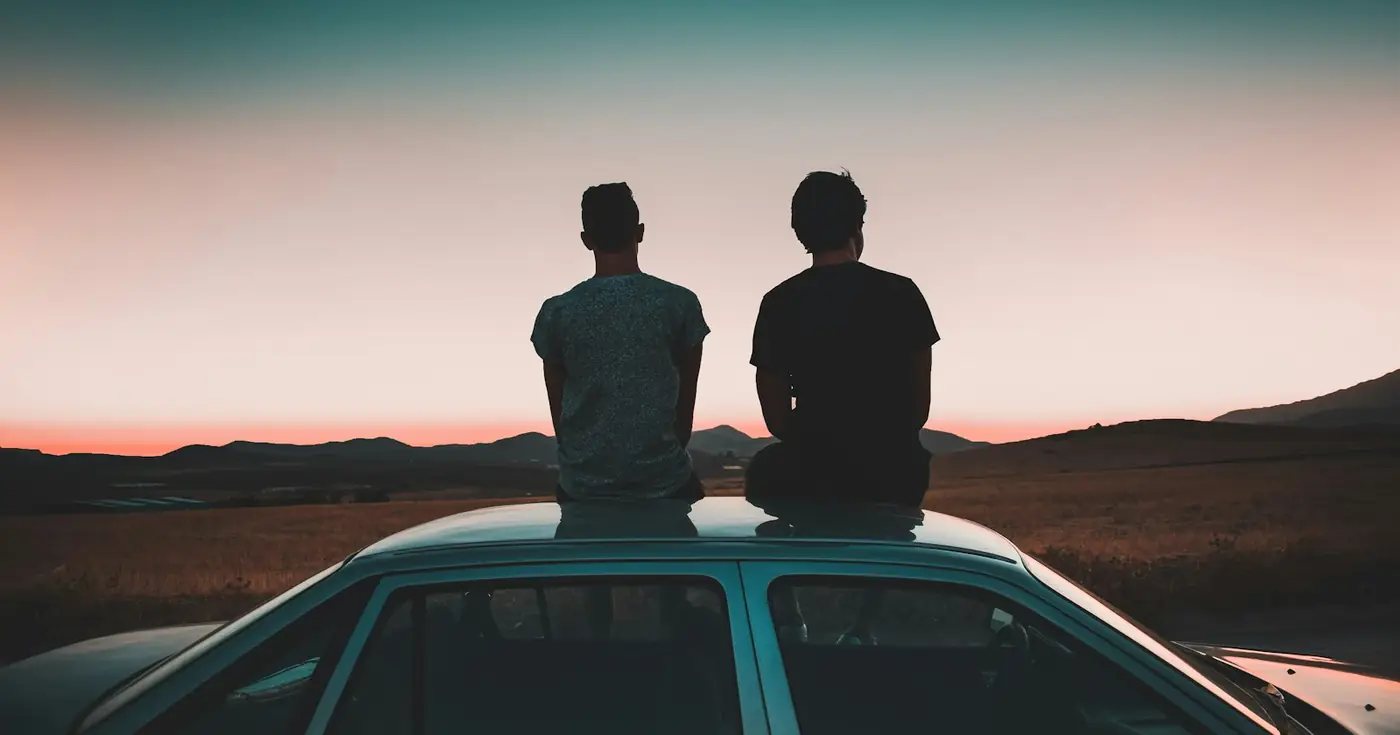 Zwei Freunde sitzen bei Sonnenuntergang auf dem Dach eines Autos
